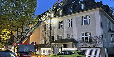 Brandbekämpfung beim Dachstuhlbrand: Gebäudeansicht mit Drehleiter 